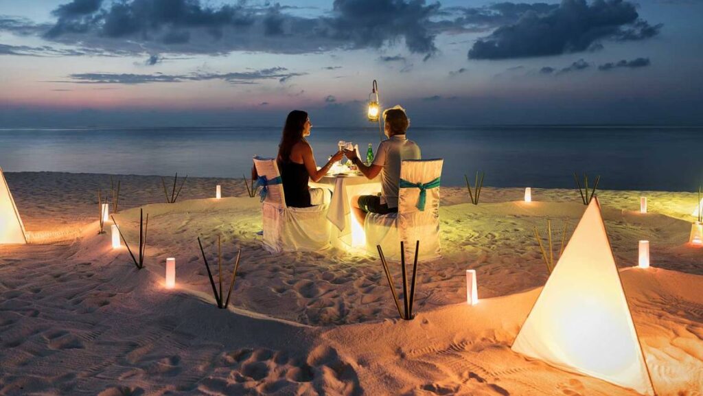 Romantic couple enjoying candlelight dinner on Goa beach at sunset.